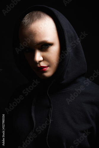 young woman with short haircut looking from the Dark. bald girl in Hood