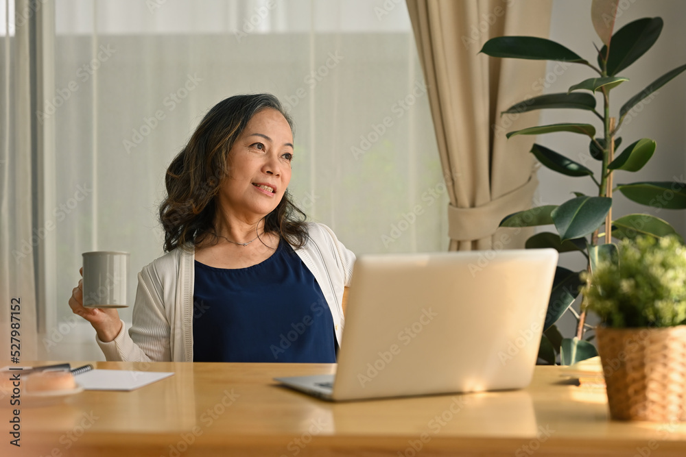 Happy beautiful relaxed mature older adult grey-haired woman relaxing with coffee drink after working at home, enjoying cozy lazy break.