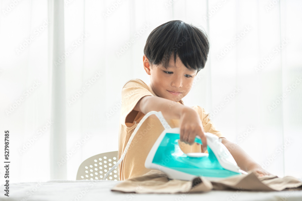 young happy boy iron his school uniform with iron on iron board at home during weekend for house cleaning family activity young happy boy iron his school uniform with iron on iron board at home during weekend for house cleaning family activity