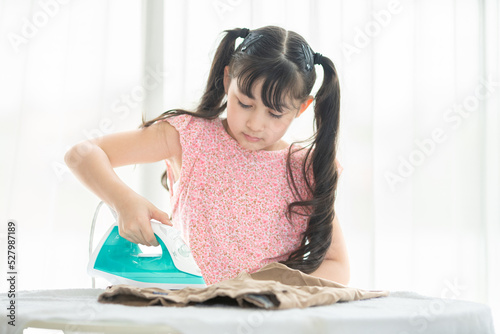 young happy girl iron her school uniform with iron on iron board at home during weekend for house cleaning family activity