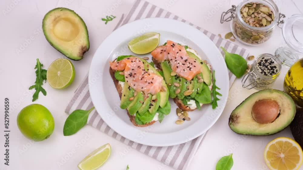 healthy breakfast or snack - woman puts plate with soft cheese, avocado and salmon sandwiches on a table