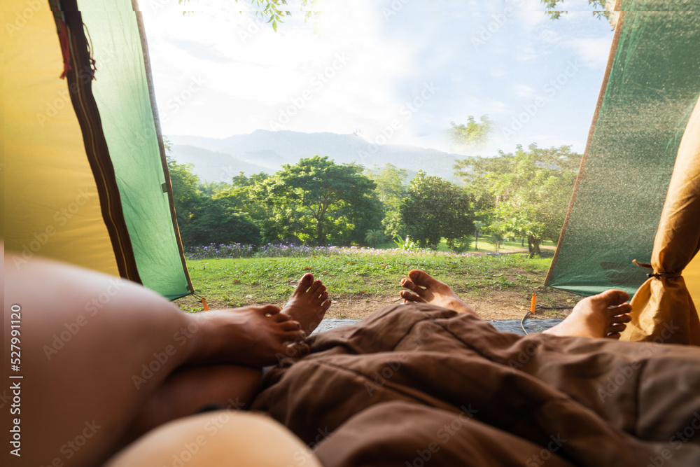 Two Traveler lying in tent and enjoying the view of sunrise, forest and mountains in the morning.