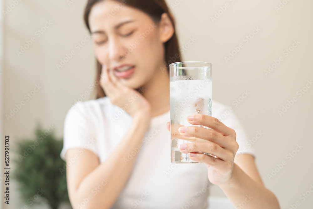 Suffering from toothache, blur asian young woman touch cheek, face expression ache or feel pain, sensitive molar teeth, hand holding glass of water with ice, inflammation when drink cold, healthcare. Suffering from toothache, blur asian young woman touch cheek, face expression ache or feel pain, sensitive molar teeth, hand holding glass of water with ice, inflammation when drink cold, healthcare.