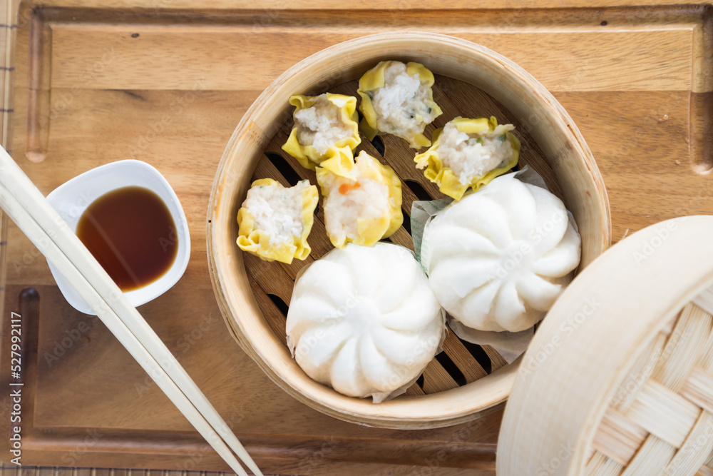Chinese steamed pork bun and dim sumis ready to eat on serving plate and steamer. Chinese steamed pork bun and dim sumis ready to eat on serving plate and steamer.