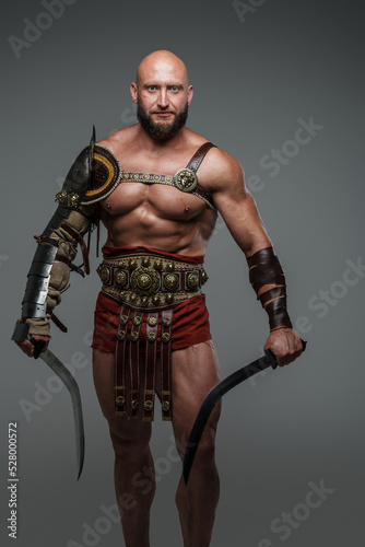 Portrait of ancient gladiator dressed in armour holding swords isolated on gray.