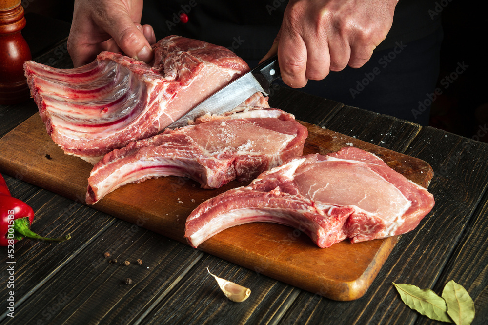 Experienced chef cuts raw meat. Butcher cutting pork ribs. Meat with bone on a wooden cutting board