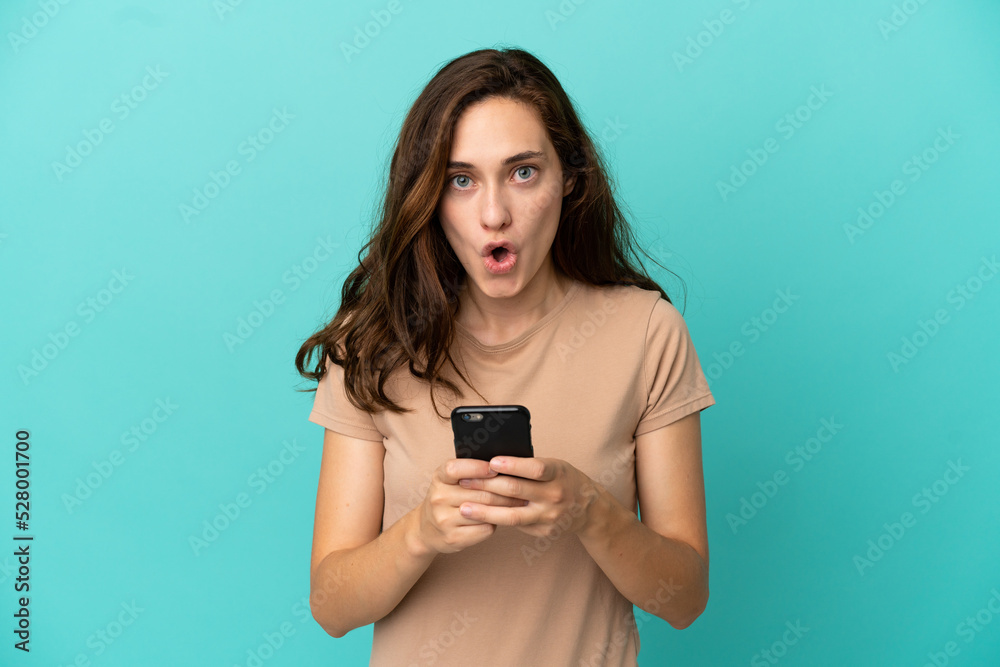 Young caucasian woman isolated on blue background looking at the camera while using the mobile with surprised expression Young caucasian woman isolated on blue background looking at the camera while using the mobile with surprised expression