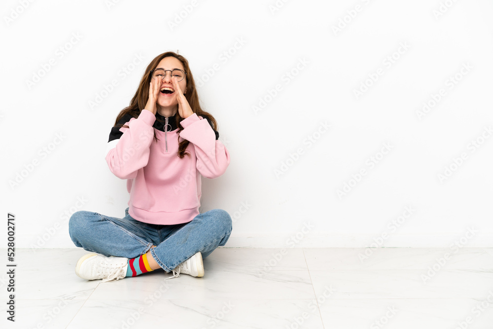 Young caucasian woman sitting on the floor isolated on white background shouting and announcing something Young caucasian woman sitting on the floor isolated on white background shouting and announcing something