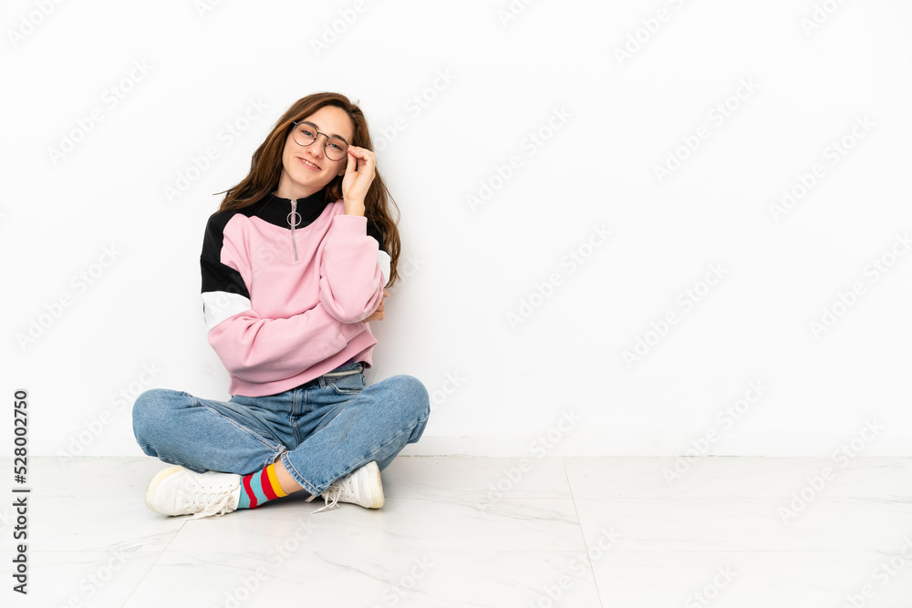 Young caucasian woman sitting on the floor isolated on white background with glasses and happy Young caucasian woman sitting on the floor isolated on white background with glasses and happy