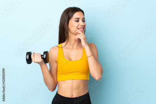 Young caucasian woman making weightlifting isolated on blue background thinking an idea and looking side