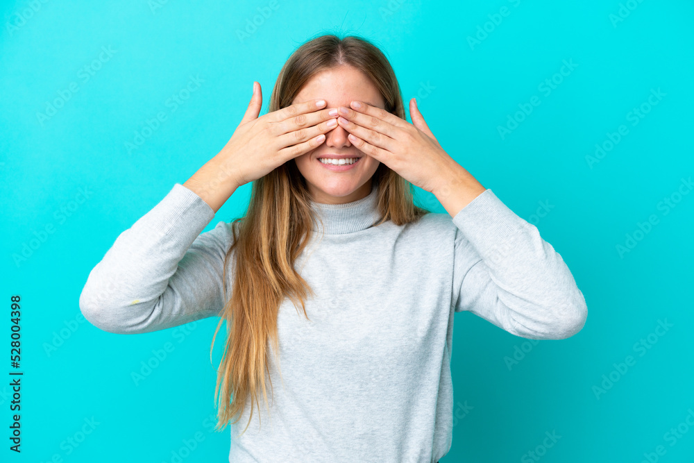 Young blonde woman isolated on blue background covering eyes by hands and smiling Young blonde woman isolated on blue background covering eyes by hands and smiling
