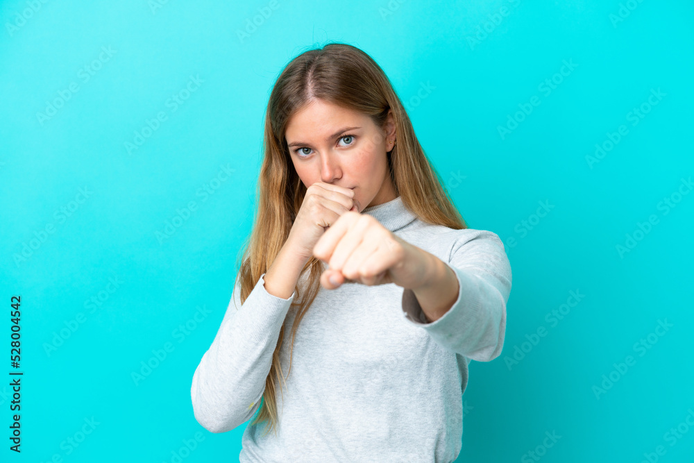 Young blonde woman isolated on blue background with fighting gesture Young blonde woman isolated on blue background with fighting gesture