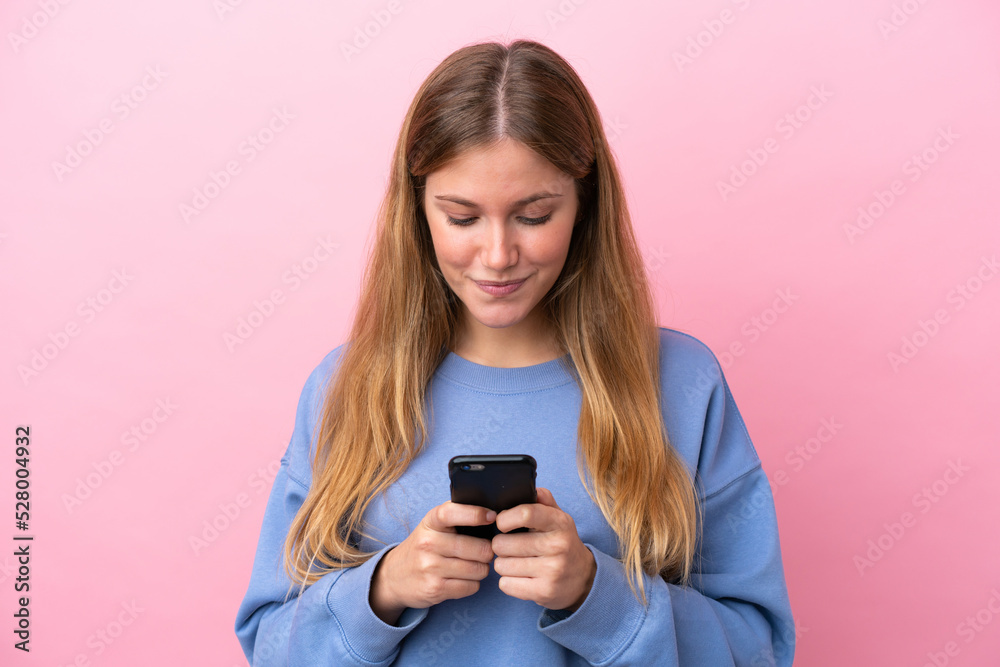 Young blonde woman isolated on pink background sending a message or email with the mobile Young blonde woman isolated on pink background sending a message or email with the mobile
