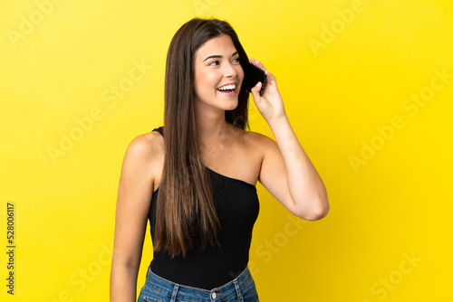 Young Brazilian woman isolated on yellow background keeping a conversation with the mobile phone