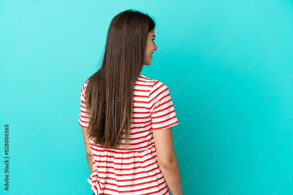Young Brazilian woman isolated on blue background in back position and looking side Young Brazilian woman isolated on blue background in back position and looking side
