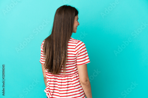 Young Brazilian woman isolated on blue background in back position and looking side