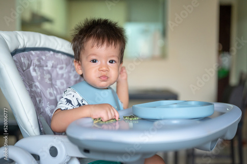 Baby boy eating by himself in his high chair at home