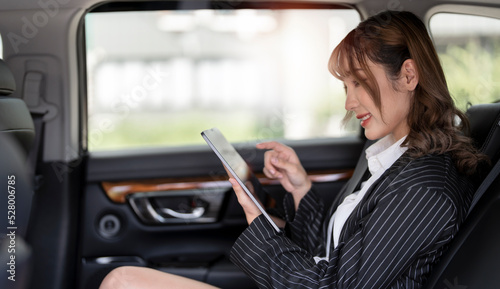Beautiful businesswoman using digital tablet while sitting on a backseat of a car.