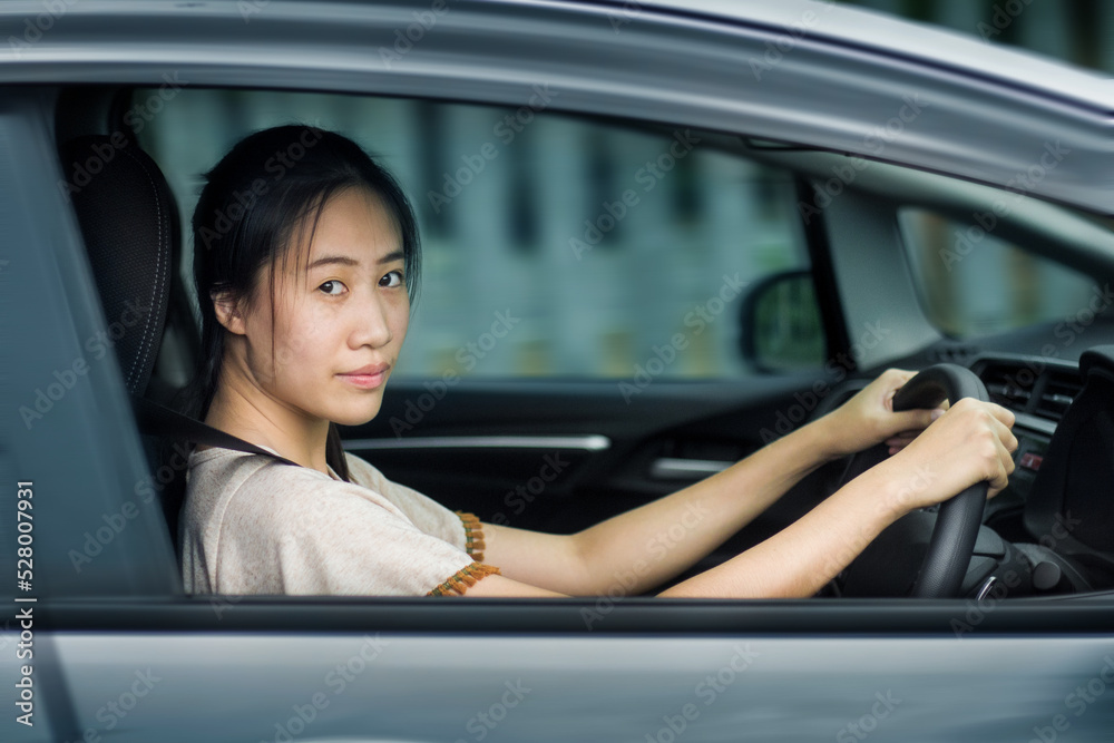 Happy Asian woman driving a car and smiling. Cute young success happy brunette woman is driving a car. Portrait of happy female driver steering car with safety belt