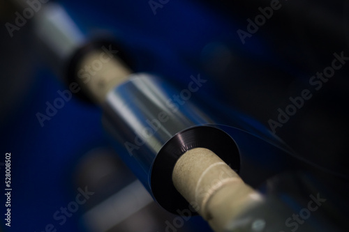 TTR ribbon on shaft of winding machine in the printing house. Black roll wax ribbon for thermal transfer for a special barcode printer. Consumables materials for barcode printing. Selective focus