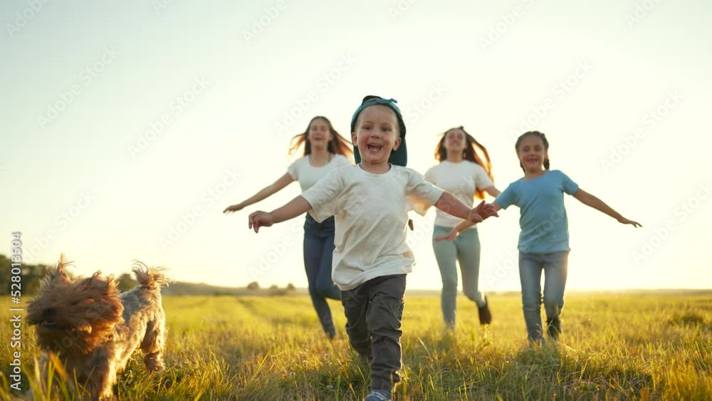 Happy family.Group of cheerful children with dog run through green grass.Family walk with dog at sunset in park.Smile of active children.Children run across field together with dog. Freedom of life Happy family.Group of cheerful children with dog run through green grass.Family walk with dog at sunset in park.Smile of active children.Children run across field together with dog. Freedom of life