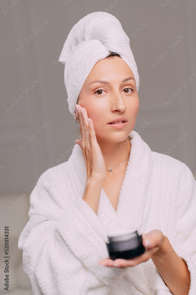 Young attractive woman in a bathrobe applies cream on her face in the bathroom. Young attractive woman in a bathrobe applies cream on her face in the bathroom.