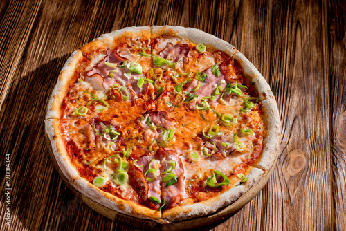 Delicious pizza with mozzarella cheese, ham, leeks on a tomato base on wood background