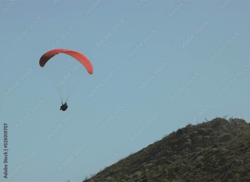 Paraglider with a red parachute flying above hills Paraglider with a red parachute flying above hills