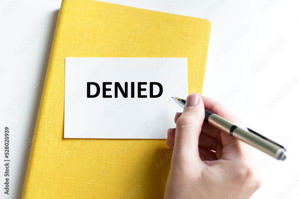Denied text on a white card that lies on a notepad, a person's hand with a pen writes text on the card Denied text on a white card that lies on a notepad, a person's hand with a pen writes text on the card