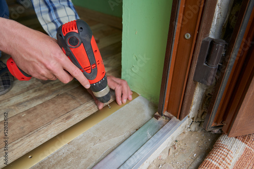 drill a hole for the dowel,a man drills a hole in the threshold of the door with a drill