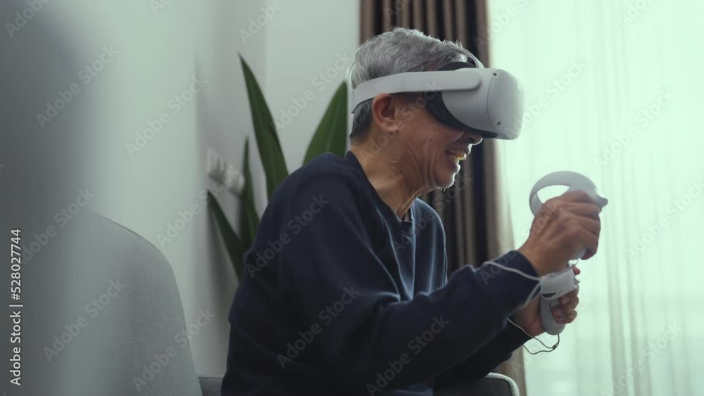 Happy senior asian man wearing vr goggle at living room. He using vr to play online game alone at home. Lifestyle, Hobbies, Technology, Entertainment concept. Happy senior asian man wearing vr goggle at living room. He using vr to play online game alone at home. Lifestyle, Hobbies, Technology, Entertainment concept.