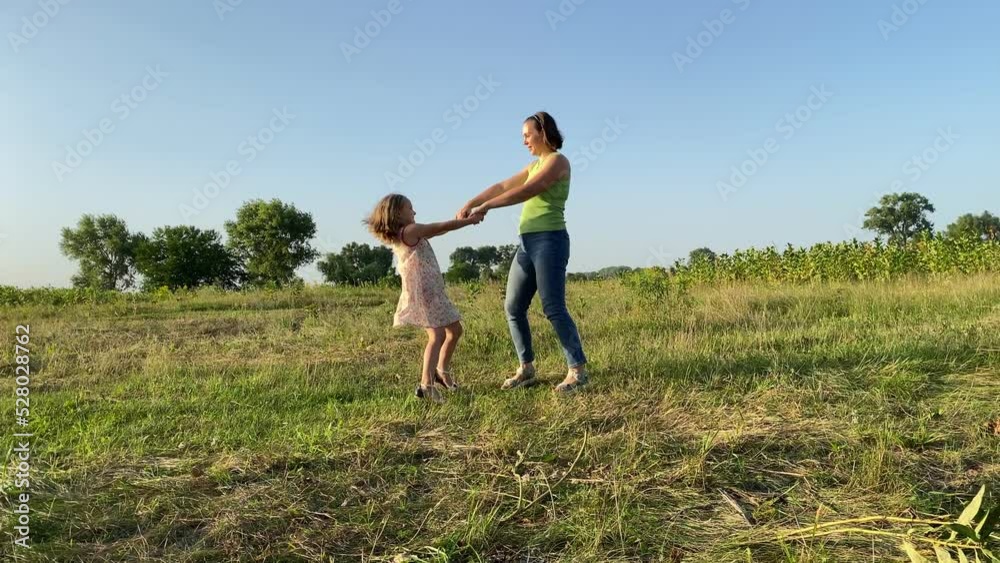 Mother, daughter having fun at meadow sunset. Young adult woman, little girl swirling around, enjoying leisure together outdoors. Cheerful mom spending playtime with child. Happiness in simple living Mother, daughter having fun at meadow sunset. Young adult woman, little girl swirling around, enjoying leisure together outdoors. Cheerful mom spending playtime with child. Happiness in simple living