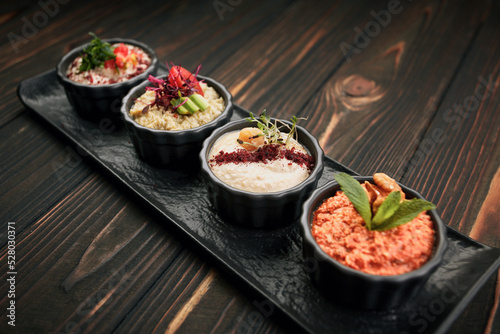 A variety of vegetable appetizers, on black plates on a wooden background