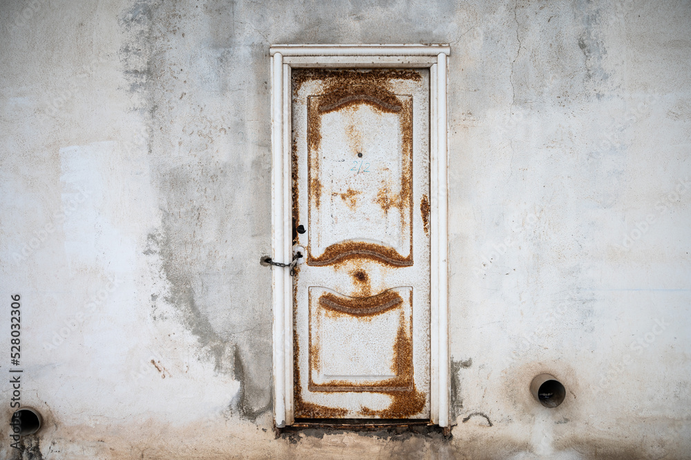 A rusty metal closed door on a white wall