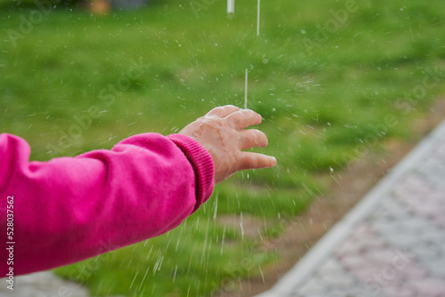 splashing water falling on a hand,a child's hand has placed its hand under the rain and is playing with water
