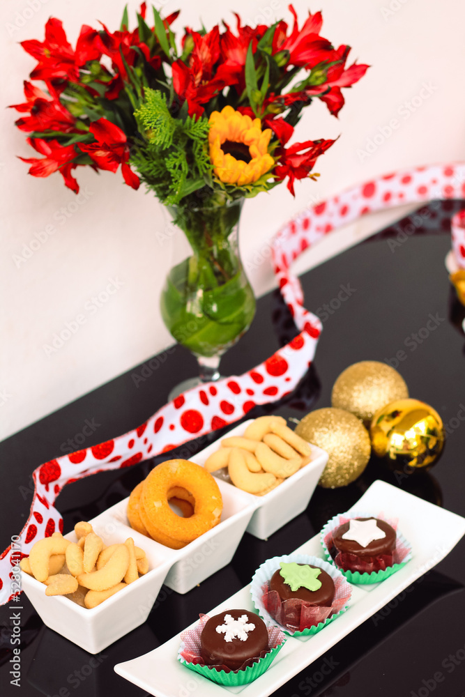 Rosquinhas com sequilhos e doces de chocolate na mesa posta com flores e bolas de natal