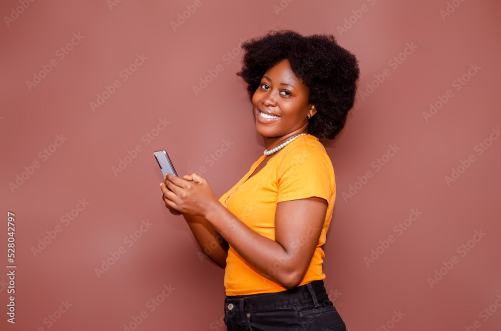 Happy excited African American lady on Afro hair style using mobile phone at studio standing behind a blank background Happy excited African American lady on Afro hair style using mobile phone at studio standing behind a blank background