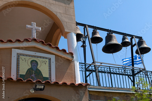 eloponnese, Greece - 18.08.2022 :Colourful mosaic hagiography of Saint Patapios ,on the facade above the entrance of the monastery with towerbell next to. sunny day with blue sky. Loutraki, Greece photo