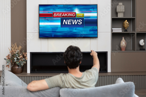 Back view on excited man sitting on the couch and watching breaking news on tv at home photo