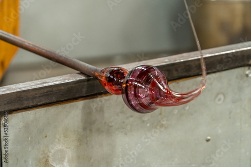 A female hand of a Glass Blower shaping molten colorful glass into a ball