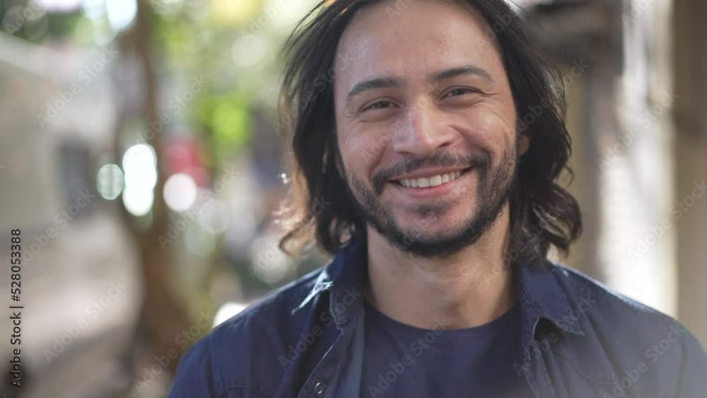 Portrait of a happy hispanic man walking forward in street. Smiling South American Brazilian person walks outdoors in urban environment in sunlight