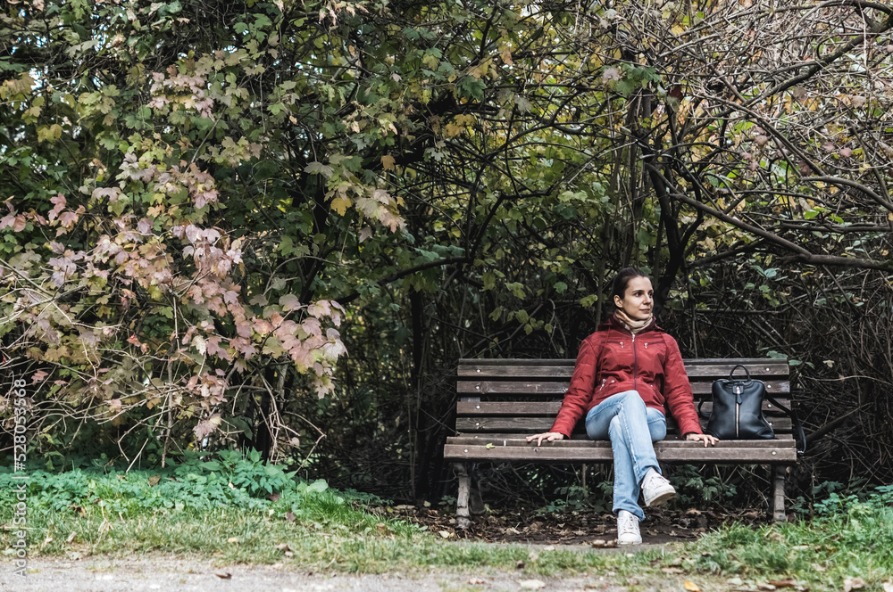 Portrait of woman sitting on bench in autumn park. Girl in red coat under tree branches Portrait of woman sitting on bench in autumn park. Girl in red coat under tree branches
