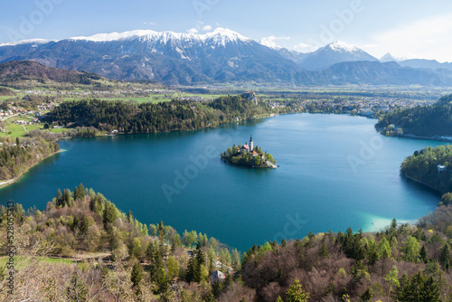 Scenic  high elevation view of famous Lake Bled in Slovenia  with snowy Julian Alps mountain range in the background  spring growth on the trees and an island with a historical church.