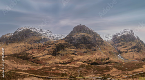 Majestic Winter landscape image of snowcapped Three Sisters mountain range in Glencoe Scottish Highands with dramatic sky