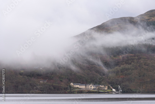 Moody dramatic misty Winter landscape drifting through trees on slopes of Ben Lomond in Scotland