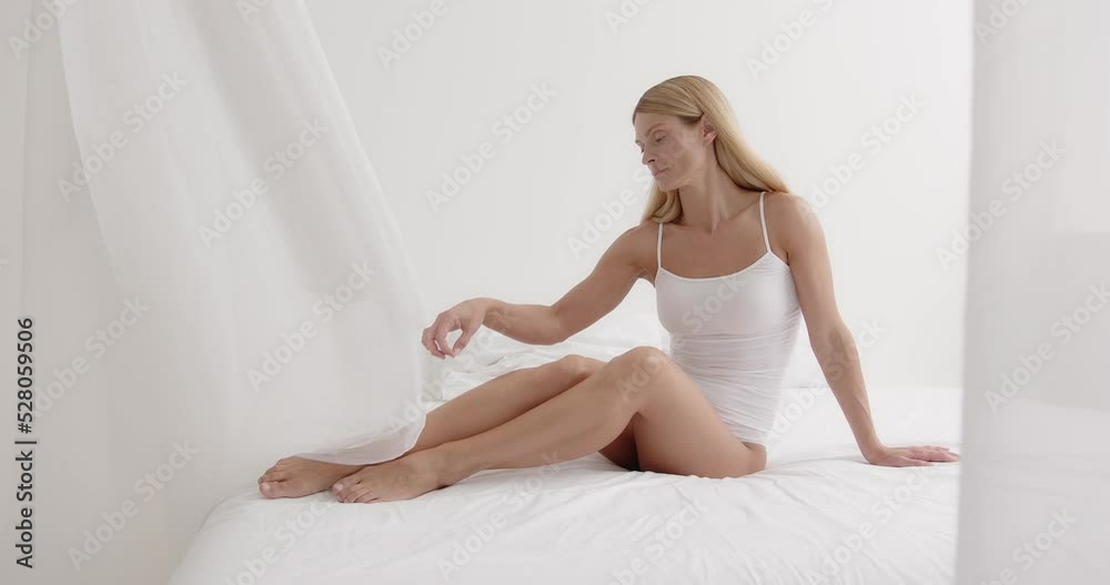Tenderness and purity. Smiling mature blonde woman touching leg with feather Tenderness and purity. Smiling mature blonde woman touching leg with feather
