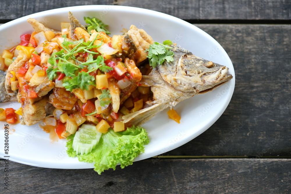 Deep-Fried snapper with Three-Flavoured Sauce. Deep Fried Fish with Chili Sauce, Pineapple, onion, tomato, carrot (all diced) topped with shredded coriander served in a white plate on a wood table.
Deep-Fried snapper with Three-Flavoured Sauce. Deep Fried Fish with Chili Sauce, Pineapple, onion, tomato, carrot (all diced) topped with shredded coriander served in a white plate on a wood table.