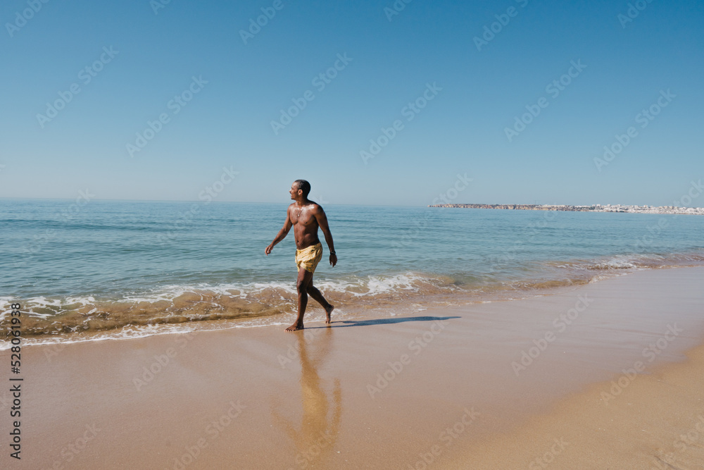 AFRICAN-AMERICAN BOY WALKING ON THE BEACH ON HIS SUNNY VACATION