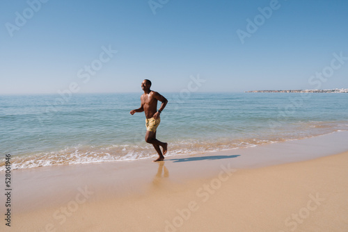 GUY RUNNING ON THE BEACH ON HIS SUNNY VACATION DOING SPORT