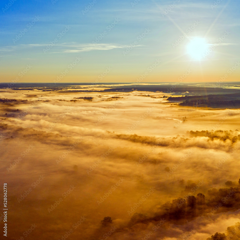 Aerial  view of a beautiful summer  landscape with a fog while dawn.  Photo from drone of a foggy landscape in spring. Top view to land while sunrise. Sun is above the horizon. Panorama.
